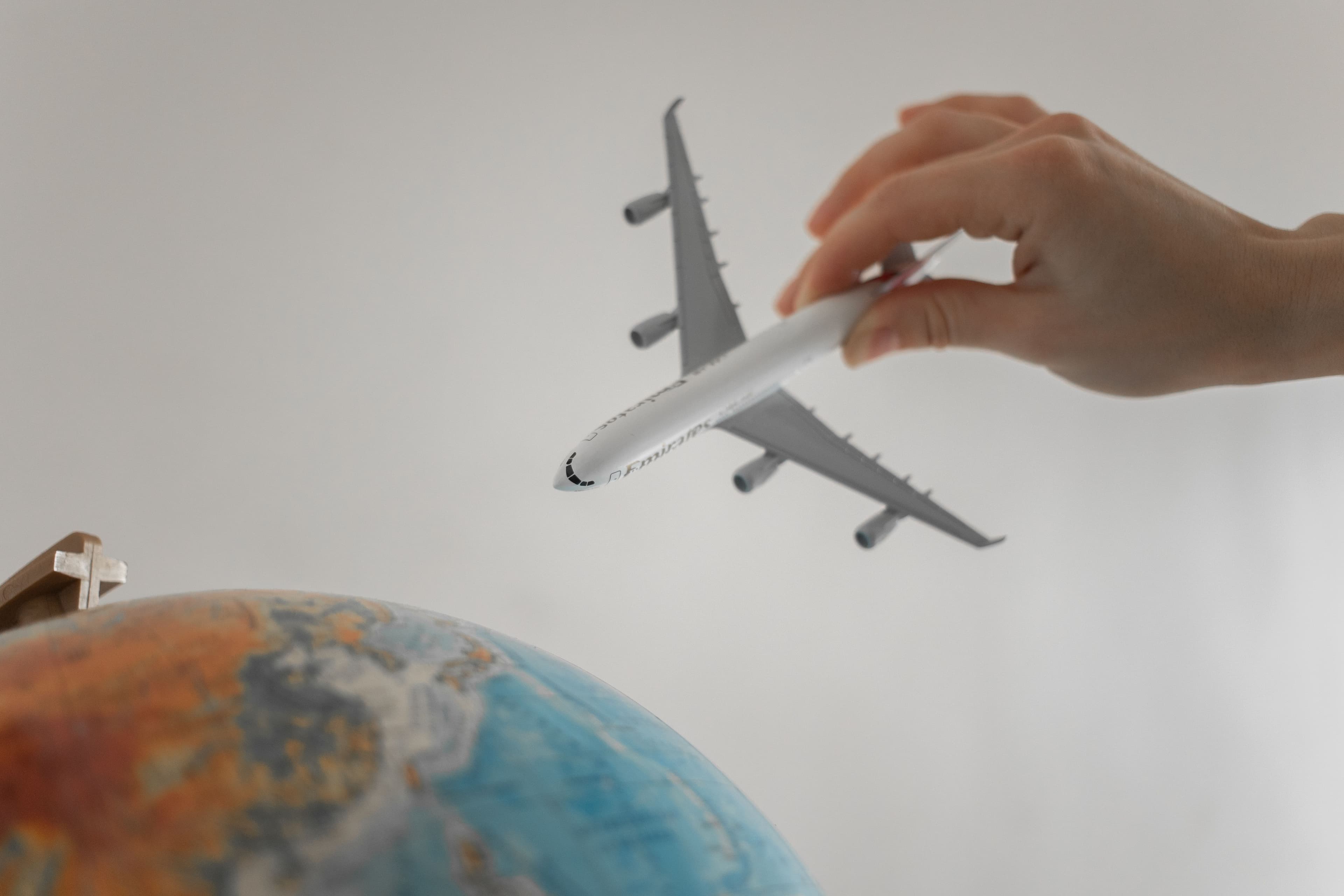 Hand holding a toy airplane above a globe, symbolizing travel for medical care