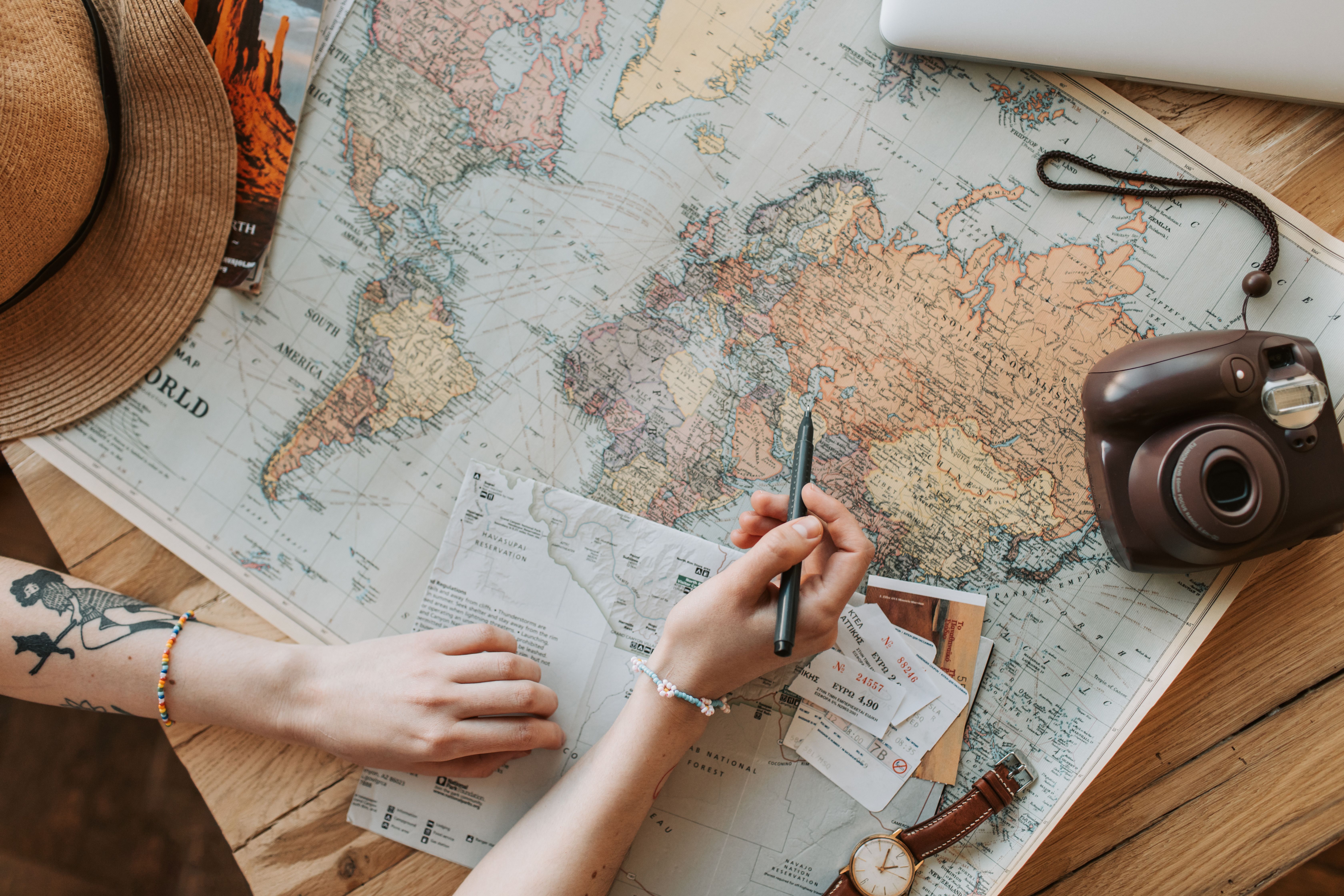 Person planning travel with a world map, tickets, and camera