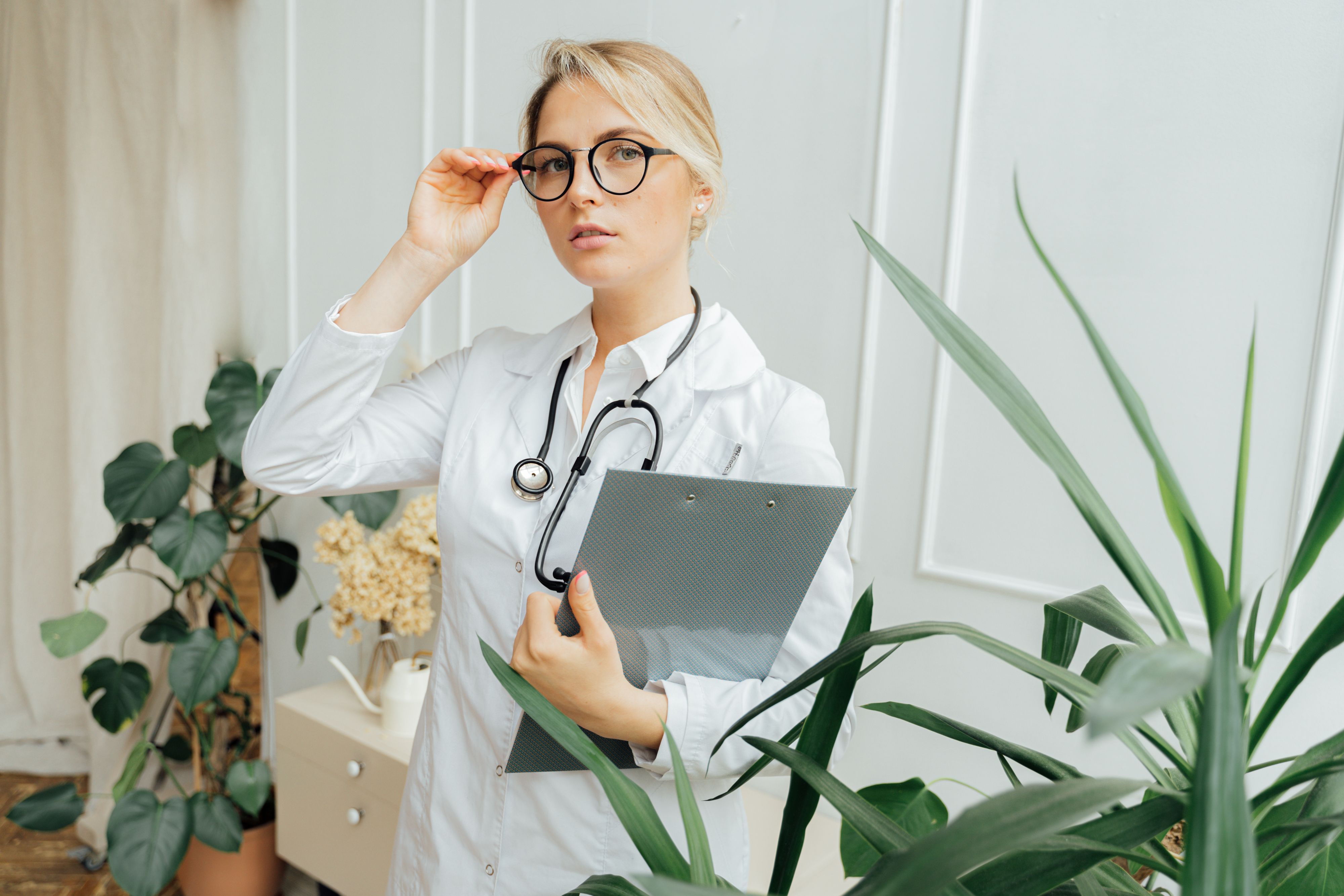 Doctor holding a clipboard, standing in a plant-filled office